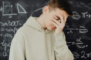 Young man overwhelmed by mathematical calculations on a blackboard in a classroom setting.