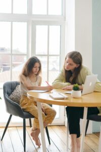 A mother helping her daughter with homeschooling in a bright, sunlit room.