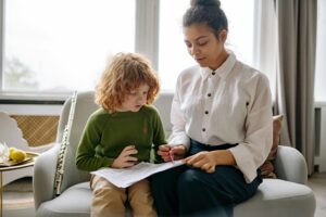 A young boy is learning music indoors with his teacher, playing the flute and reading sheet music.
