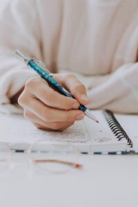 A student's hand writing notes in a copy during a personalized home tutoring session in Islamabad.