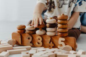 A child's hands stacking wooden counting rods to learn numbers 1, 2, 3 in a Montessori home tutoring session in Islamabad.