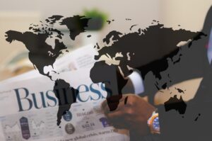 A professional hand pointing to a world map laid over a newspaper with the headline "Business," symbolizing expert Business Studies tutoring.